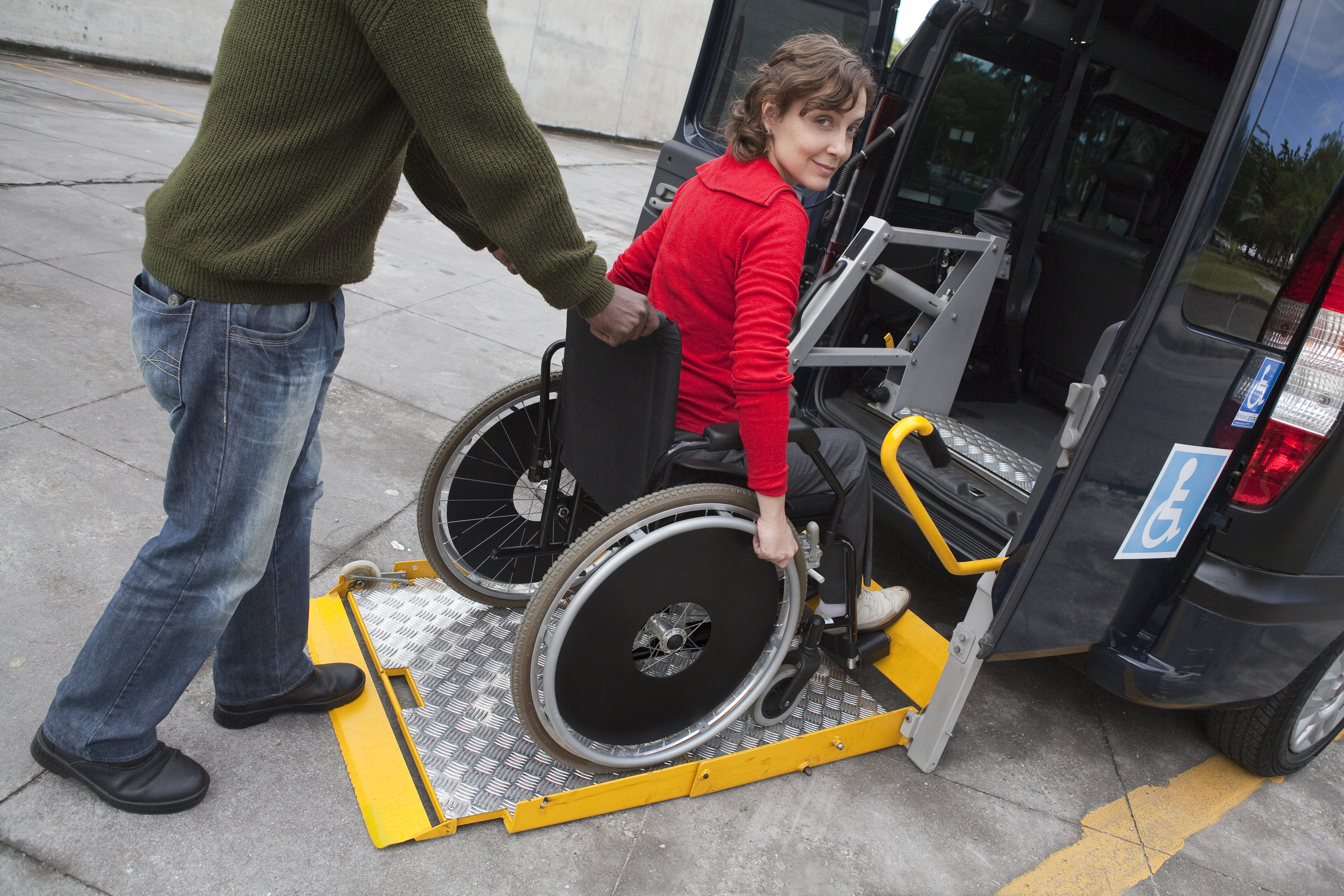 A Woman In A Wheelchair Is Helped Off A Van Using A Chair Lift